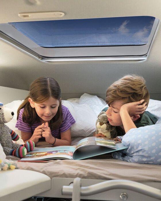 Duas crianças deitam-se na cama de um VW Grand California e lêem um livro.