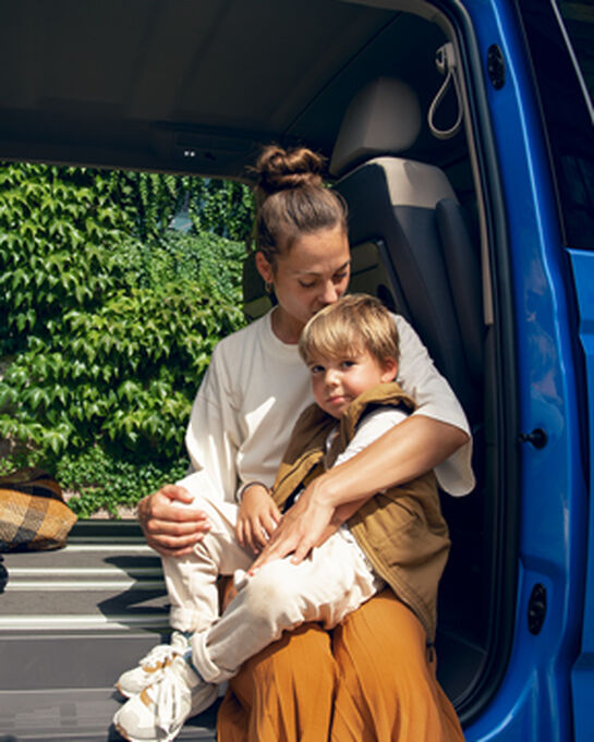Eine Mutter sitzt mit ihrem Sohn im Rahmen einer offenen Schiebetür des neuen VW Multivan T7 2021.