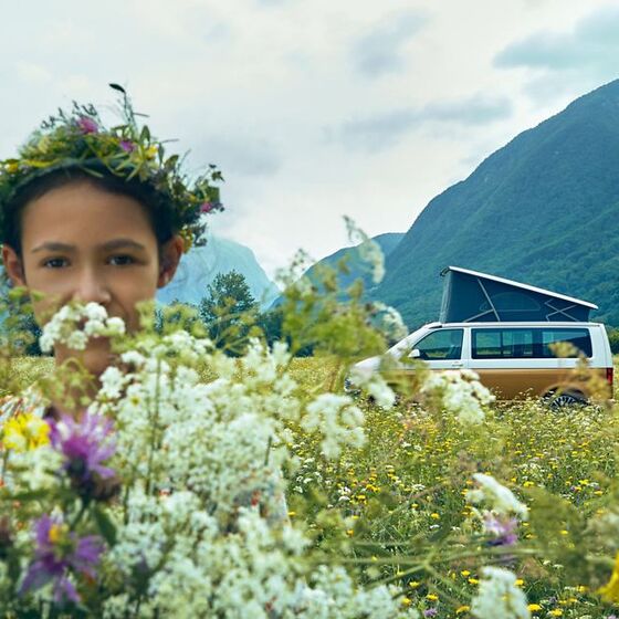 Jovem de pé sobre um prado de flores. Uma VW California pode ser vista em segundo plano.
