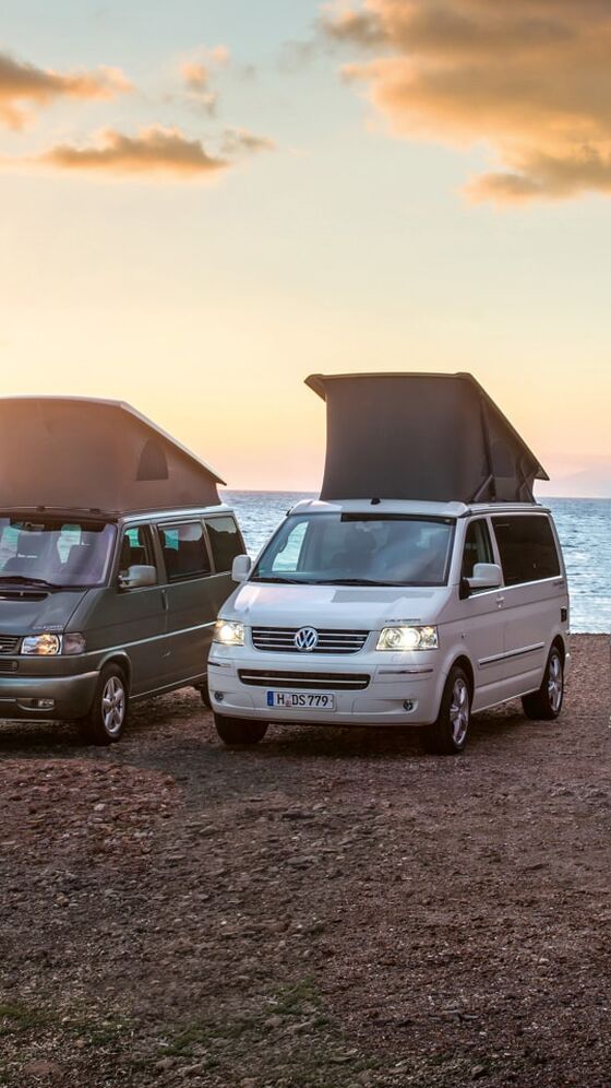 Quatro California da Volkswagen Veículos Comerciais de diferentes gerações ao pôr do sol, na praia.