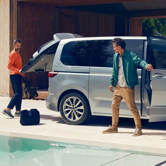 Zwei Männer stehen mit Gepäck neben dem neuen VW Multivan T7 2021.