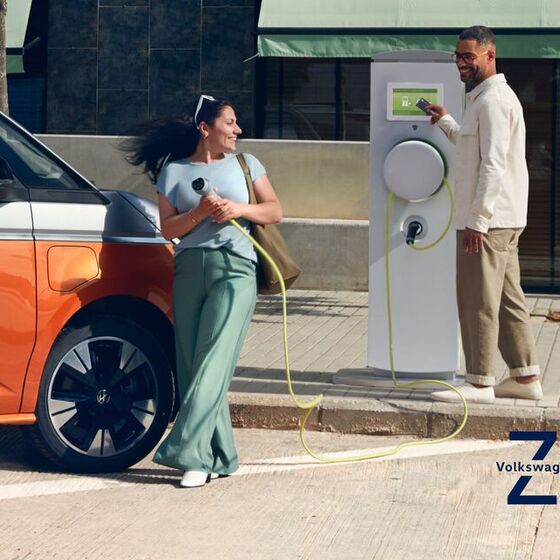 Ein Mann und eine Frau stehen an einer Ladesäule neben dem neuen VW Multivan T7 eHybrid.