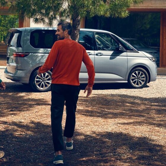 Dois homens correm para uma VW Multivan Life estacionado.