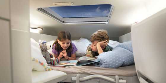 Duas crianças deitam-se na cama de trás na VW Grand California.