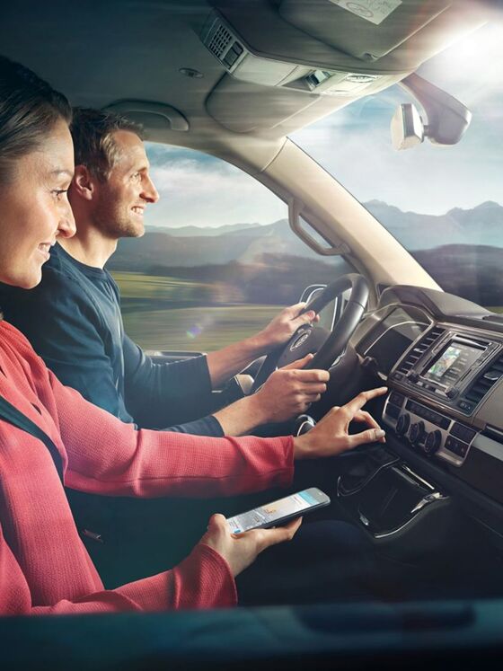 Eine Frau und ein Mann sitzen in einem VW Nutzfahrzeug, die Frau tippt gerade auf das Display