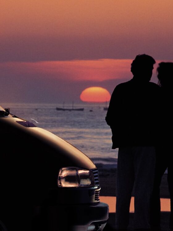 Um casal a observar o pôr do sol na praia com a sua California da Volkswagen Veículos Comerciais