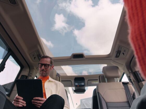 homem sentado com computador portátil no interior da nova VW Multivan e o tecto panorâmico de vidro pode ser visto.